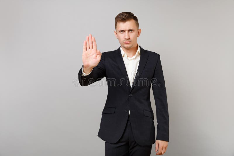 经典黑衣服的,衬衣陈列与在灰色墙壁上隔绝的棕榈的中止姿态冷漠年轻商人 免版税库存照片 经典黑衣服的,衬衣陈列与在灰色墙壁上隔绝的棕榈的中止姿态冷漠年轻商人 免版税库存照片